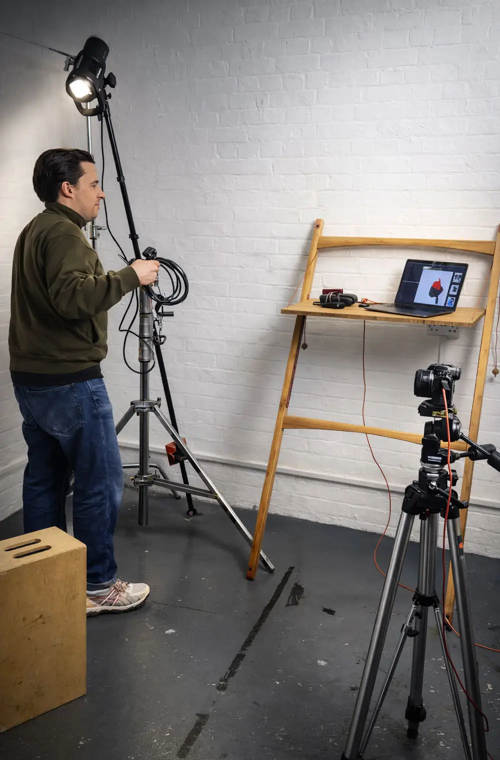 Portable desk for photographers setup with laptop tethered to camera, studio lighting, and tripod in a professional photography workspace